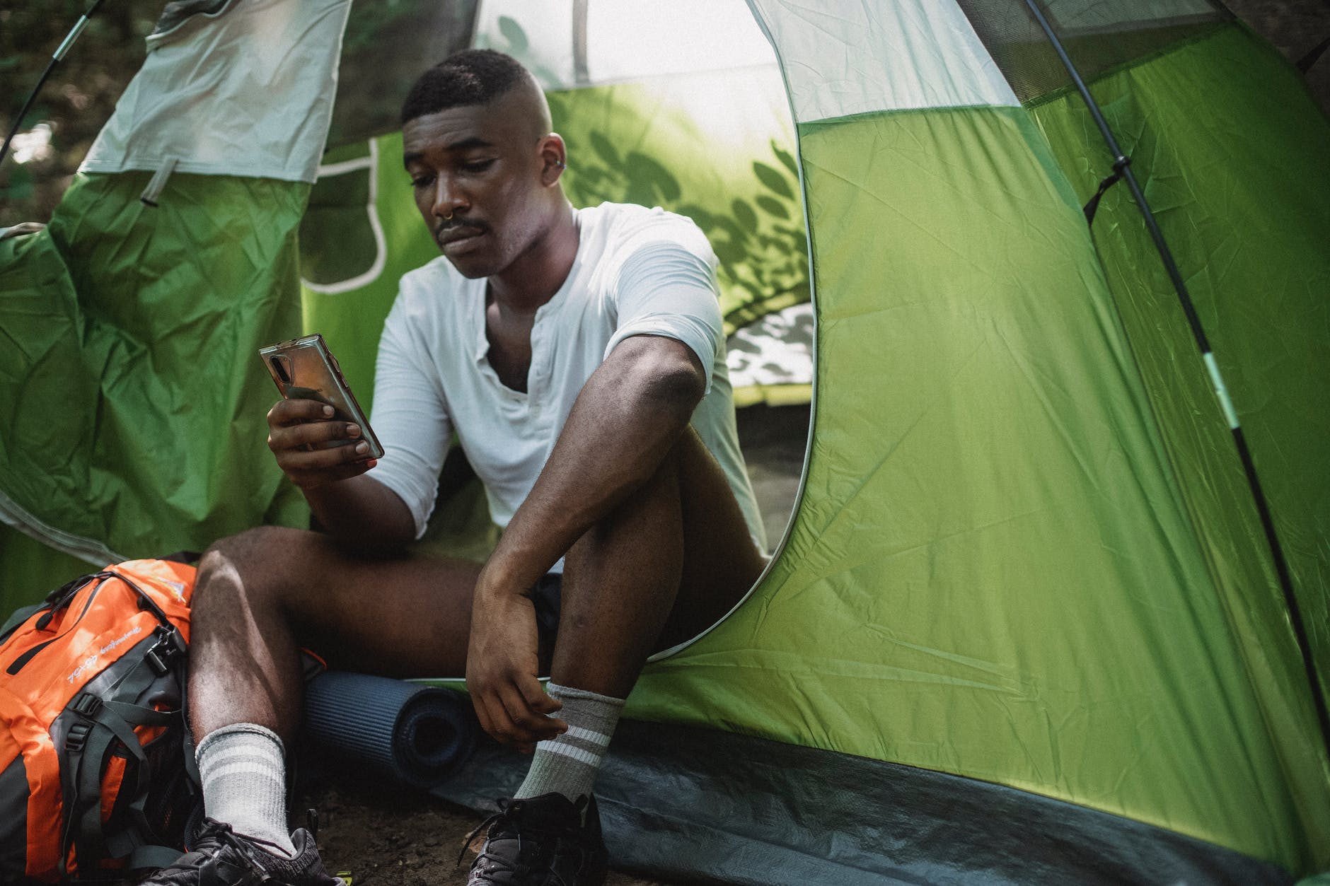 unhappy black man surfing smartphone in tent