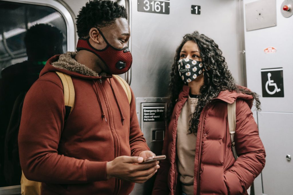 multiethnic couple in masks with smartphone talking on subway